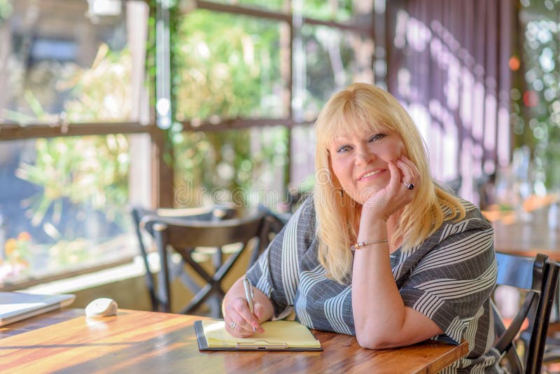 Mezzo elegante del ritratto invecchiato più seduta della donna di dimensione e che fa le note al suo diario sul balcone o sul ter fotografia stock Mezzo elegante del ritratto invecchiato più seduta della donna di dimensione e che fa le note al suo diario sul balcone o sul ter fotografia stock