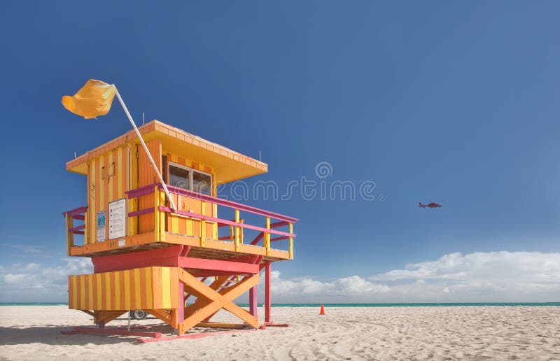 Miami Beach Florida, lifeguard house in a typical colorful Art Deco style on a sunny summer day, with blue sky and Atlantic Ocean in the background. Rescue helicopter is patrolling the beach. World famous travel location.