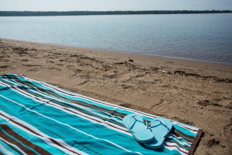 Lake Michigan shoreline beach with blue beach towel and flip flops. Lake Michigan shoreline beach with blue beach towel and flip flops