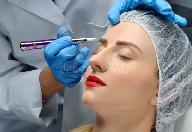 Microblading Cosmetologist que hace maquillaje permanente Mujer atractiva que consigue las cejas faciales del cuidado y del tatua imagen de archivo libre de regalías Microblading Cosmetologist que hace maquillaje permanente Mujer atractiva que consigue las cejas faciales del cuidado y del tatua imagen de archivo libre de regalías