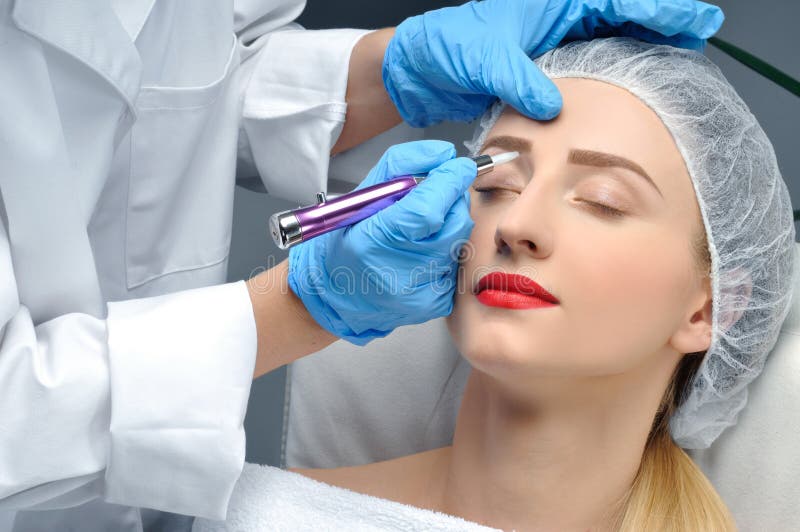 Microblading Cosmetologist que hace maquillaje permanente Mujer atractiva que consigue las cejas faciales del cuidado y del tatua imagenes de archivo Microblading Cosmetologist que hace maquillaje permanente Mujer atractiva que consigue las cejas faciales del cuidado y del tatua imagenes de archivo