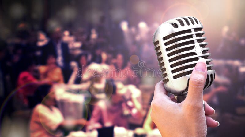 Microphone and singer on stage concept - Close up vintage microphone in singer hand singing on stage of wedding event party or business meeting with lighting effect and copy space. Microphone and singer on stage concept - Close up vintage microphone in singer hand singing on stage of wedding event party or business meeting with lighting effect and copy space