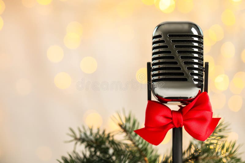 Microphone with red bow and fir branches against blurred lightst. Christmas music