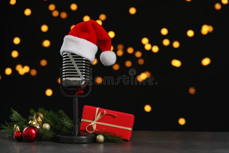 Microphone with Santa hat and decorations on table against blurred lights, space for text. Christmas music