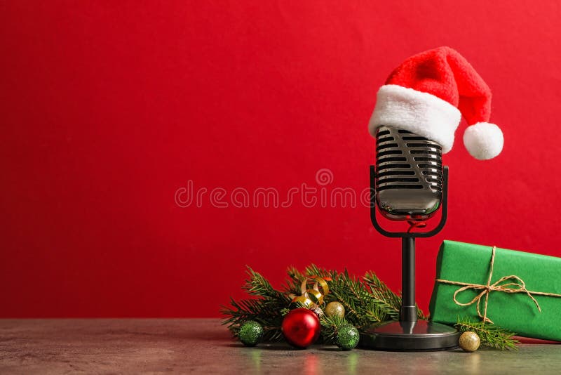 Microphone with Santa hat and decorations on grey table against red background. Christmas music