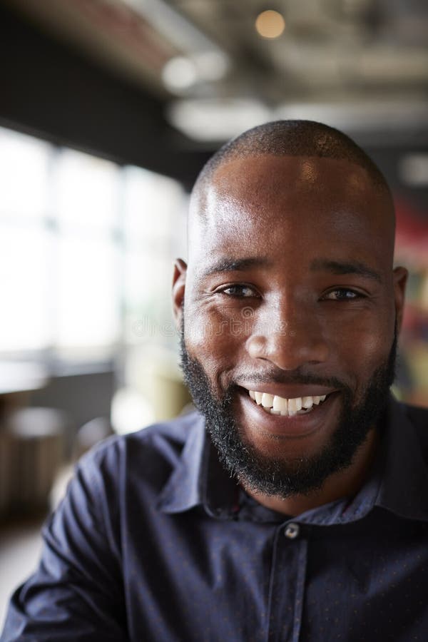 Mid adult black male creative sitting in an office social area, head and shoulders close up, vertical, crop stock image Mid adult black male creative sitting in an office social area, head and shoulders close up, vertical, crop stock image