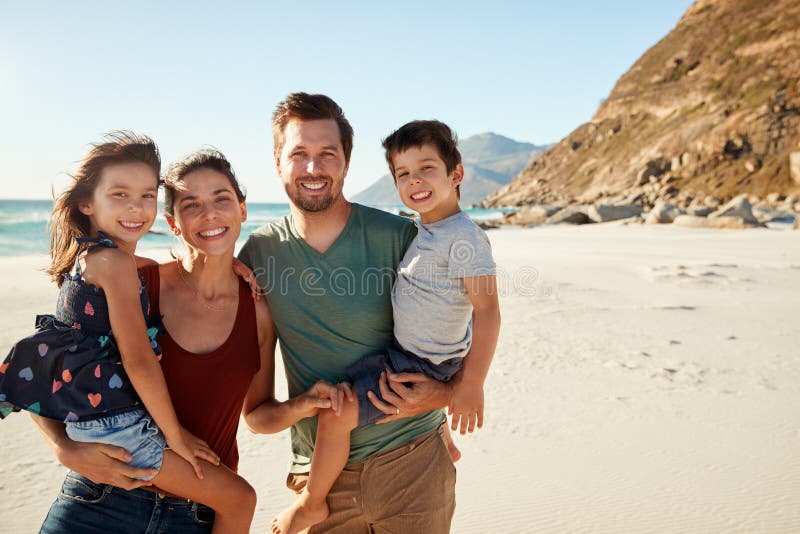 Mid adult white couple standing on a beach each carrying one of their children, front view, close up