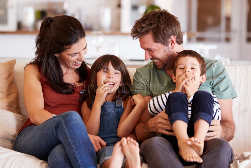 Mid adult white couple and their two young children sitting on a sofa at home smiling at each other