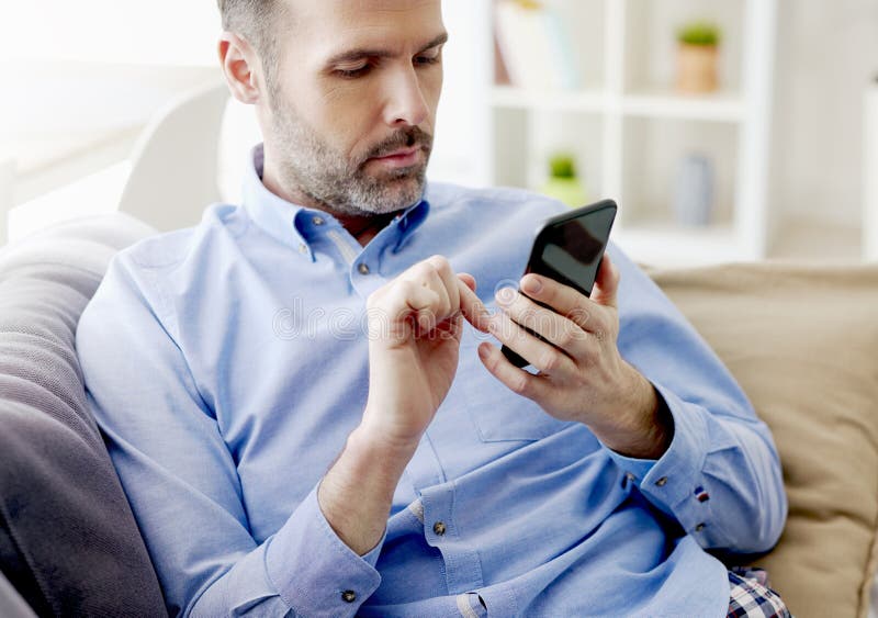 Man Sitting on Sofa and Browsing a Phone Stock Photo Image of room