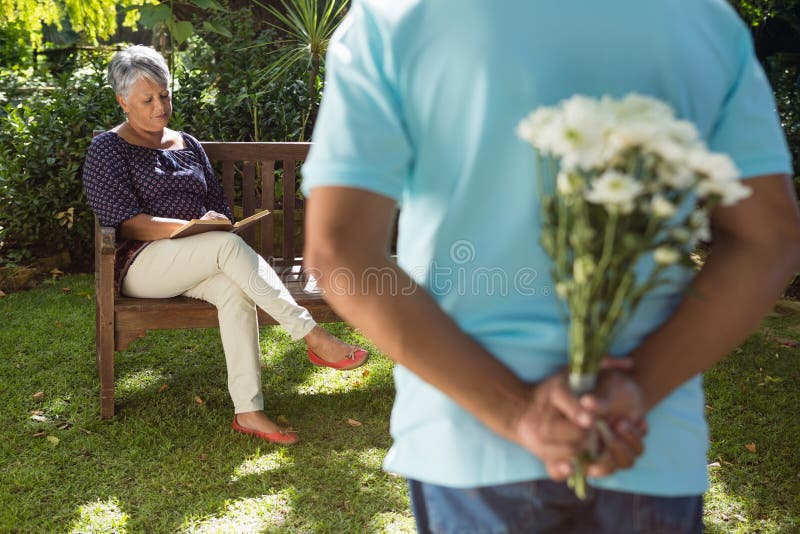 Mid-section of senior men hiding flowers behind back in garden. Mid-section of senior men hiding flowers behind back in garden