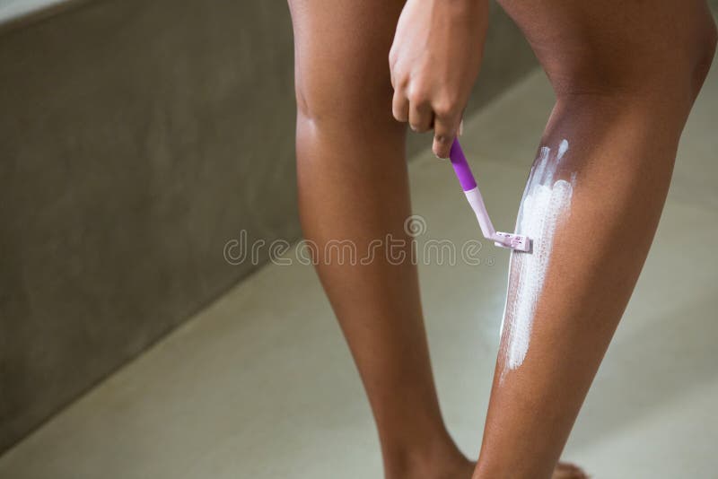 Mid section of woman shaving leg.