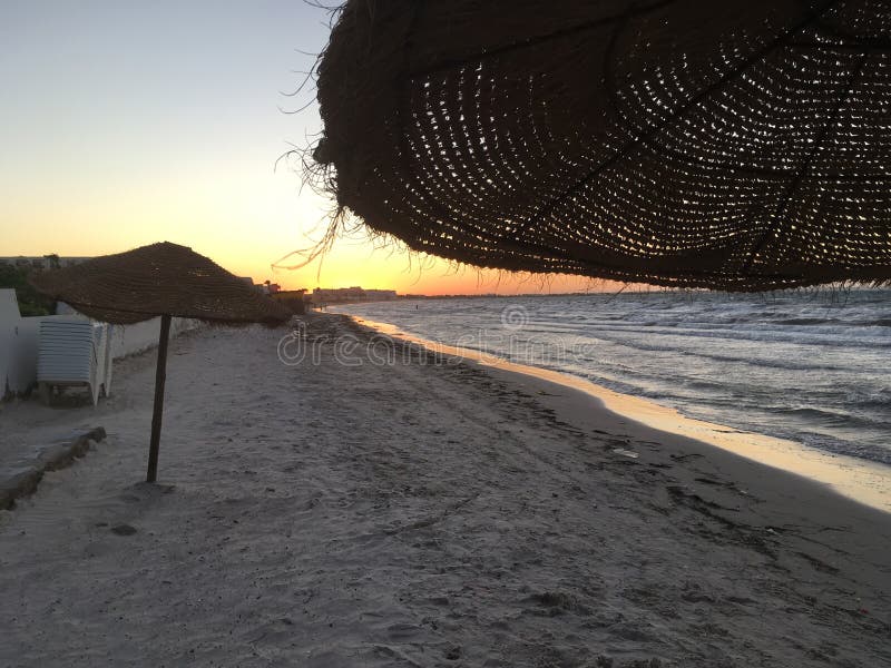 Middellandse Zee, strand, zonsondergang, rieten paraplu's en golven stock afbeelding Middellandse Zee, strand, zonsondergang, rieten paraplu's en golven stock afbeelding