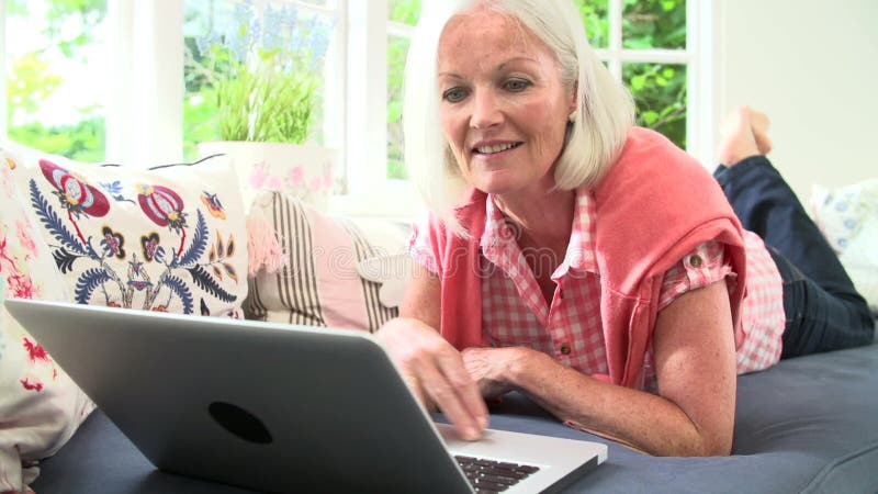 Midden Oude Vrouw die Laptop met behulp van die op Bank liggen