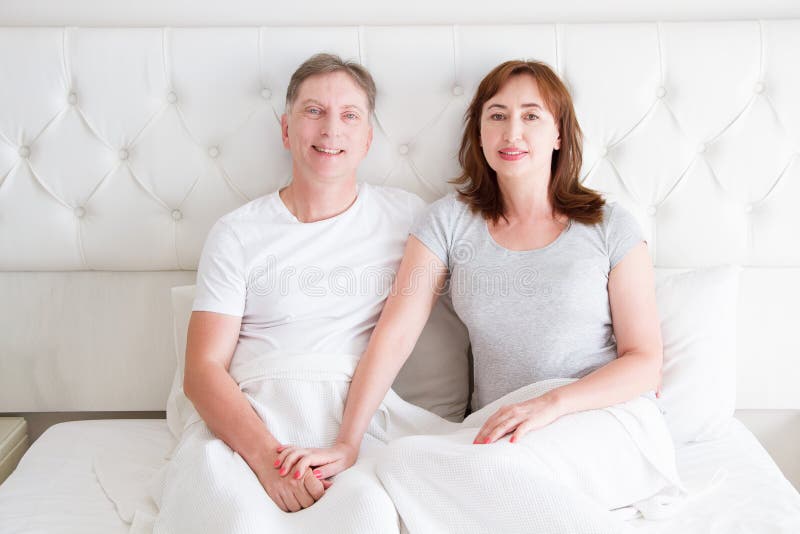 Middle age couple with wrinkles sitting in bed. Template blank t shirt. Woman and man in bedroom. Healthy lifestyle and sleep royalty free stock photography Middle age couple with wrinkles sitting in bed. Template blank t shirt. Woman and man in bedroom. Healthy lifestyle and sleep royalty free stock photography