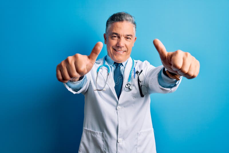 Middle age handsome grey-haired doctor man wearing coat and blue stethoscope approving doing positive gesture with hand, thumbs up