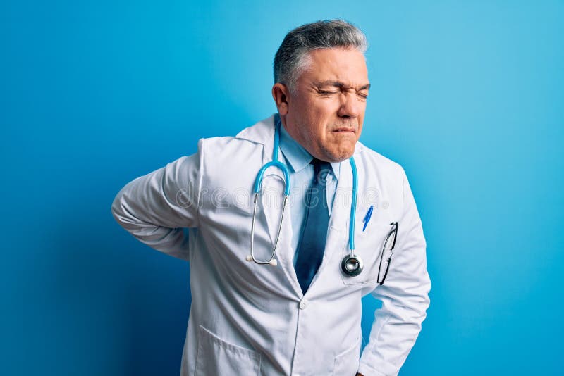 Middle age handsome grey-haired doctor man wearing coat and blue stethoscope Suffering of backache, touching back with hand