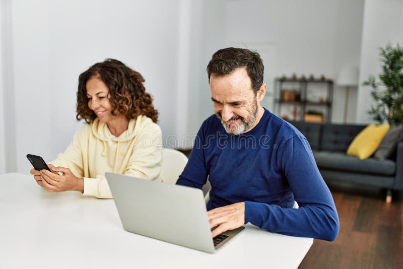 Middle age hispanic couple smiling happy using laptop and smartphone at home stock photography