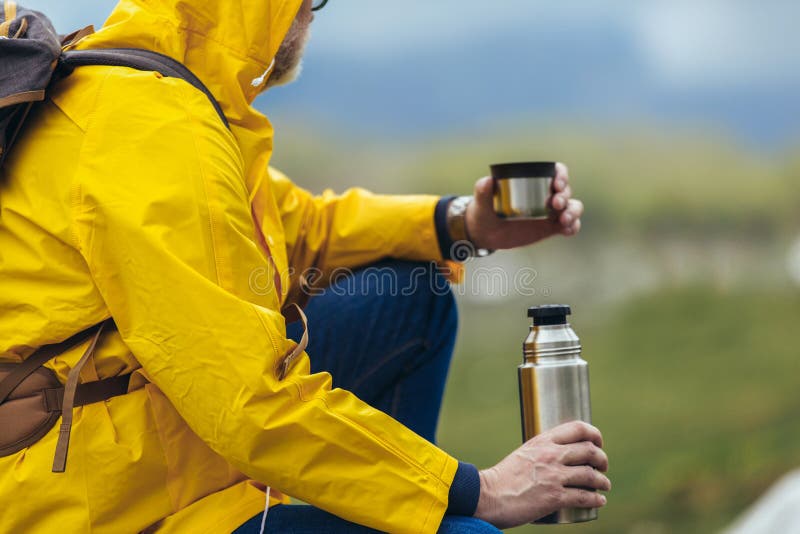 Man with backpack taking break of hiking in a beautiful nature and taking tea or water from a thermos flask