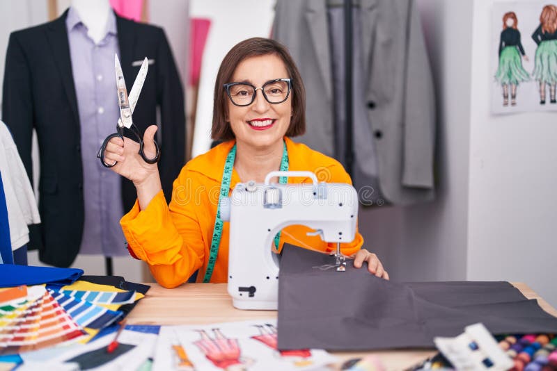 Middle Age Woman Tailor Using Sewing Machine Holding Scissors at Tailor