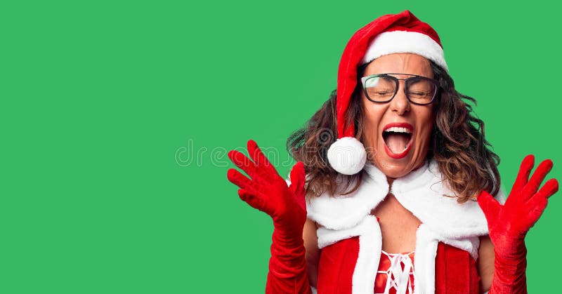 Middle age woman wearing Santa Claus costume celebrating mad and crazy for success with arms raised and closed eyes screaming