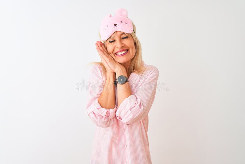 Middle age woman wearing sleep mask and pajama over isolated white background sleeping tired dreaming and posing with hands