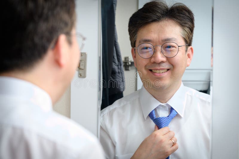 Middle-aged Asian businessman smiling while looking at the mirror in the morning