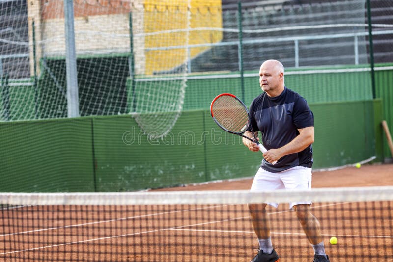 A middle-aged bald man plays tennis on the outdoor court. Sunny day royalty free stock image A middle-aged bald man plays tennis on the outdoor court. Sunny day royalty free stock image