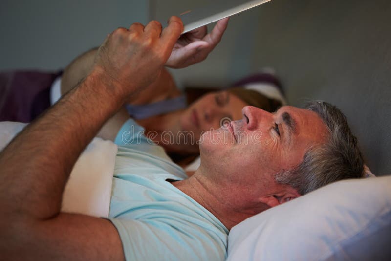 Middle Aged Couple In Bed With Man Using Tablet Computer stock image Middle Aged Couple In Bed With Man Using Tablet Computer stock image