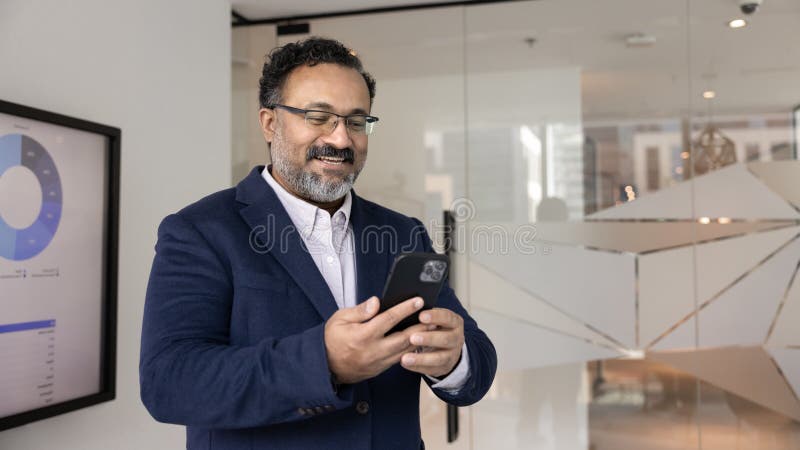 Middle-aged Indian businessman in suit using smartphone in office royalty free stock photos