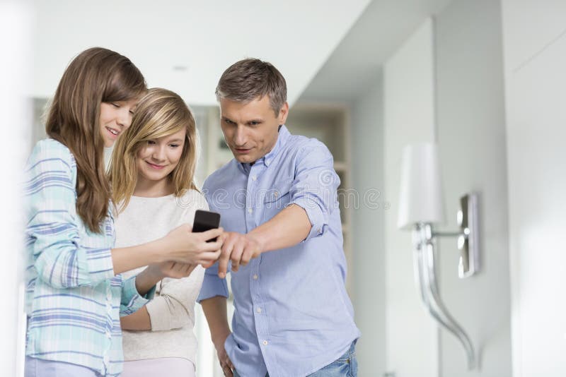 Middle-aged man with daughters using smart phone at home stock photo Middle-aged man with daughters using smart phone at home stock photo