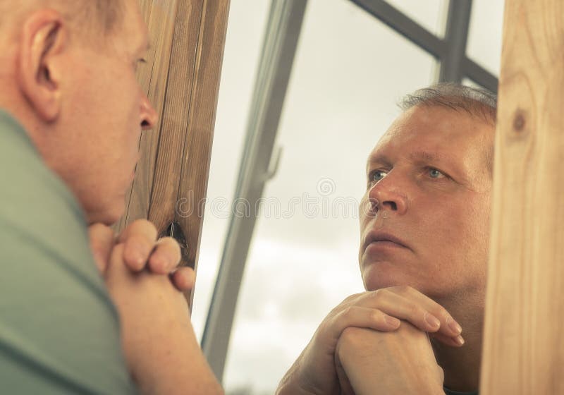 Middle-aged man looking at mirror reflection seriously, thinking about his age and life