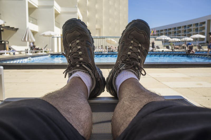 Middle aged man on swimning pool sunlounger wearing trekking shoes. Inappropriate shoes for summer