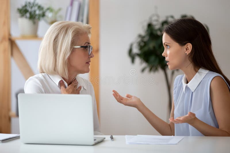 Middle-aged and millennial female colleagues having different opinions on joint project arguing seated at workplace, negative attitude, inequality and discrimination, poor work environment concept. Middle-aged and millennial female colleagues having different opinions on joint project arguing seated at workplace, negative attitude, inequality and discrimination, poor work environment concept