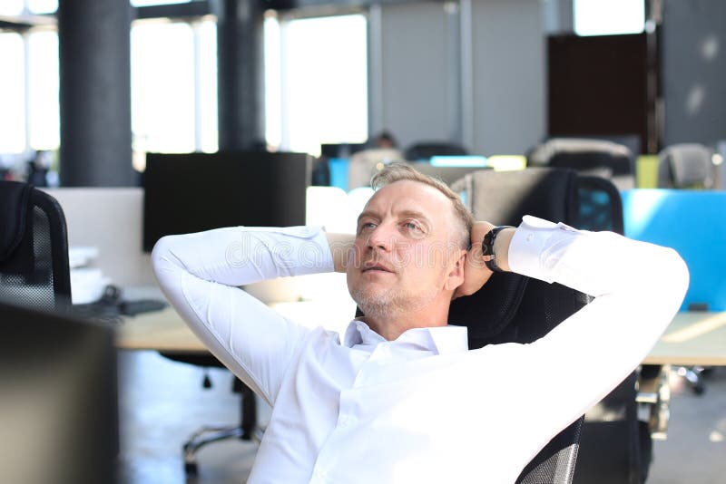 Middle aged modern businessman keeping hands behind head and smiling while sitting in the office stock image Middle aged modern businessman keeping hands behind head and smiling while sitting in the office stock image