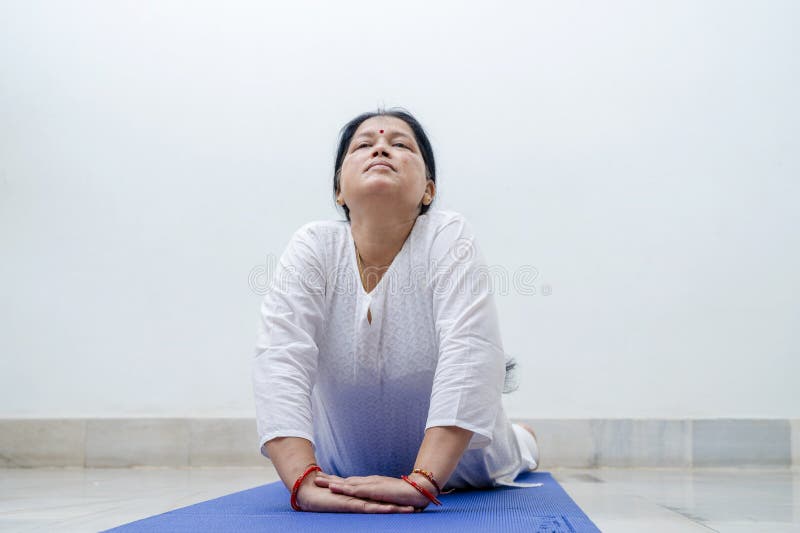 Middle Aged or an Old Indian Woman Performing Yoga Early Morning, in her house in white dress. Stay Home Stay Safe and Fit