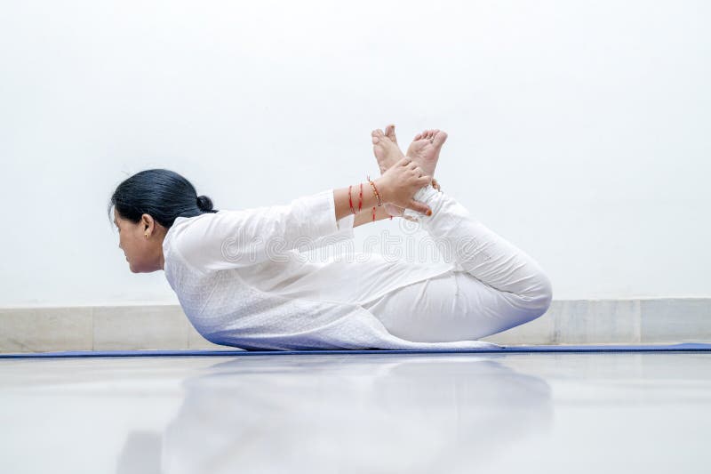 Middle Aged or an Old Indian Woman Performing Yoga Early Morning, in her house in white dress. Stay Home Stay Safe and Fit