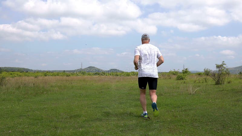 Middle aged sporty man running on the meadow in springtime