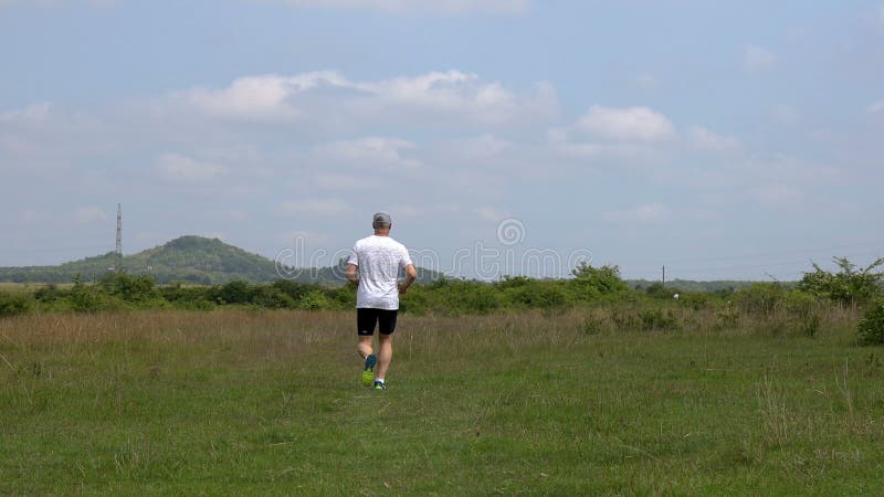 Middle aged sporty man running on the meadow in springtime