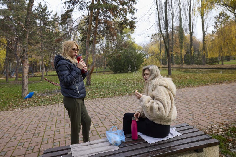 Woman and her friend are talking and drinking coffee in the park on a bench royalty free stock images