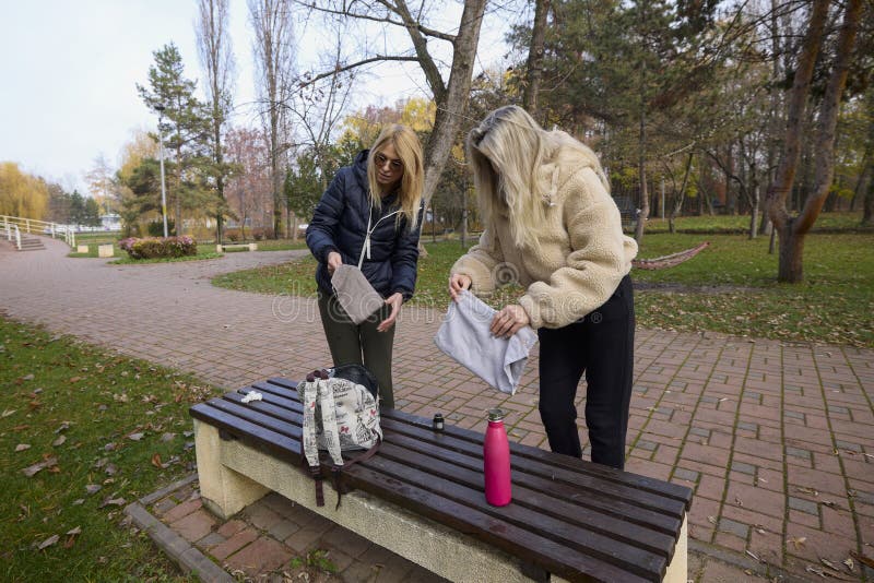 Woman and her friend are talking and drinking coffee in the park on a bench stock photo