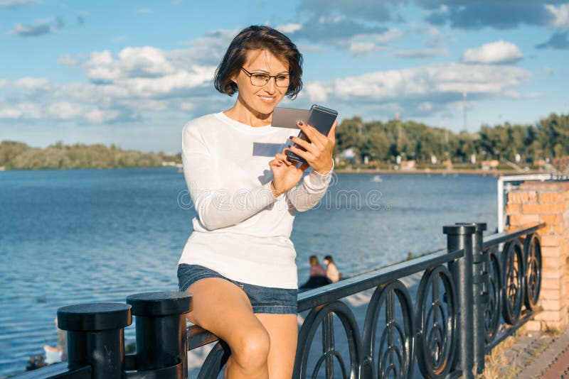 Middle-aged woman with mobile phone and business card. Female uses smartphone looking at the card stock photos Middle-aged woman with mobile phone and business card. Female uses smartphone looking at the card stock photos