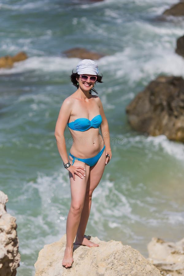 Middle aged woman in panama posing on rocky seashore.