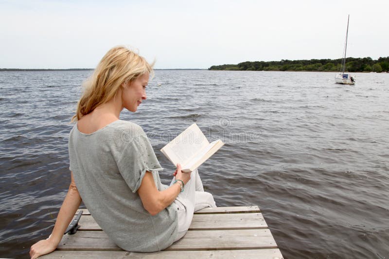 Middle-aged woman reading book by the lake