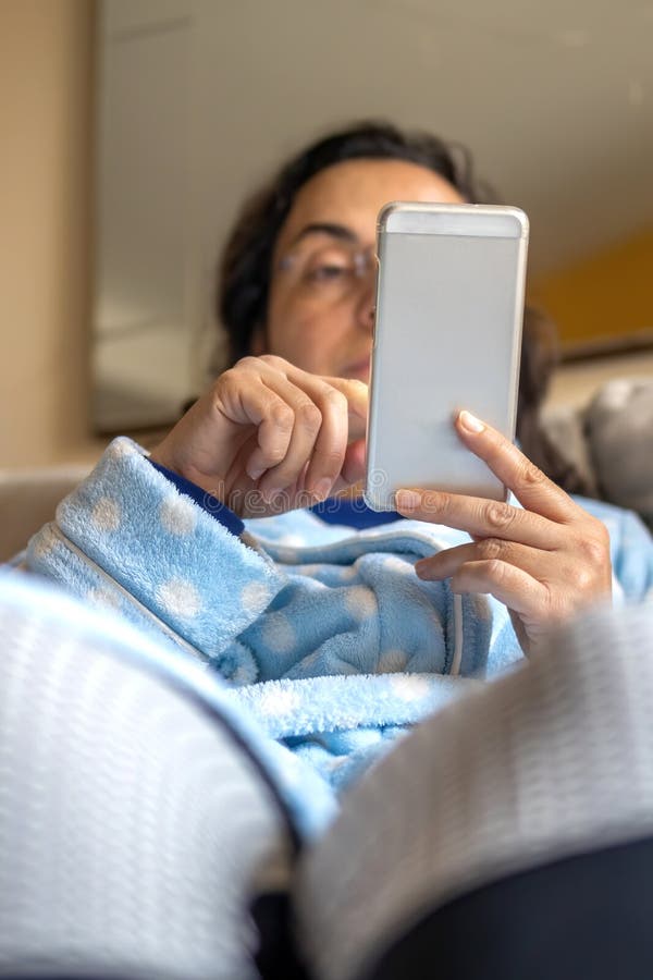 Middle-aged woman relaxing at home on the sofa reading her text messages on her mobile phone