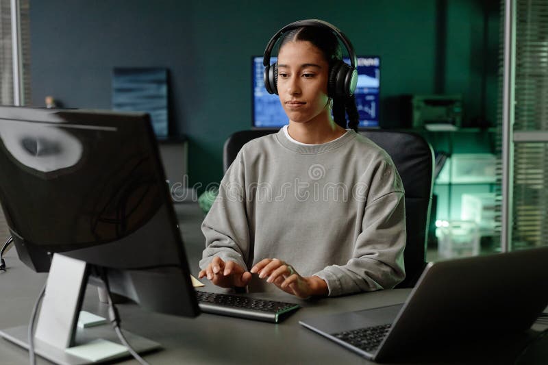 Middle Eastern Female Programmer in Headphones Using Computer at Workstation in Office stock photography