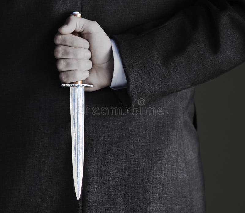 Closeup midsection of businessman holding knife against black background. Closeup midsection of businessman holding knife against black background