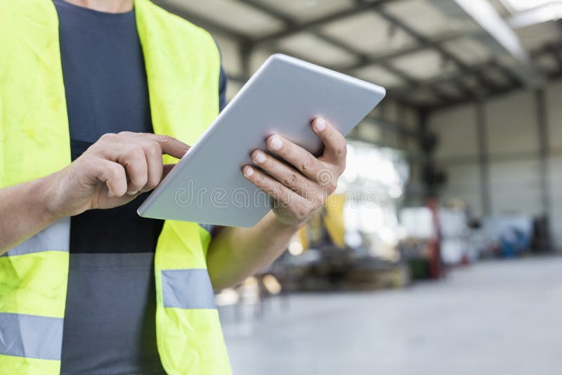 Midsection av den manuella arbetaren som använder den digitala minnestavlan i metallbransch royaltyfri bild Midsection av den manuella arbetaren som använder den digitala minnestavlan i metallbransch royaltyfri bild