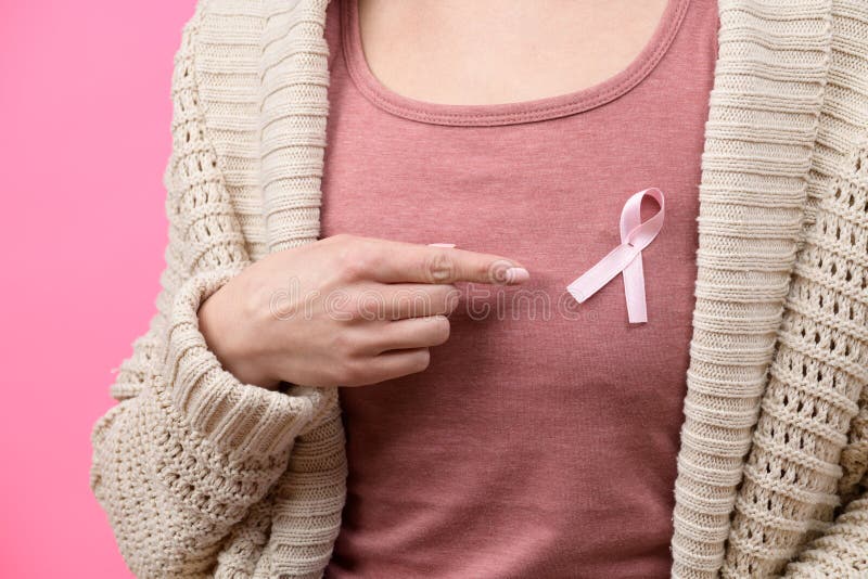 Midsection of a woman pointing to a pink breast cancer awareness ribbon on her Tshirt isolated over pastel pink background. royalty free stock images Midsection of a woman pointing to a pink breast cancer awareness ribbon on her Tshirt isolated over pastel pink background. royalty free stock images