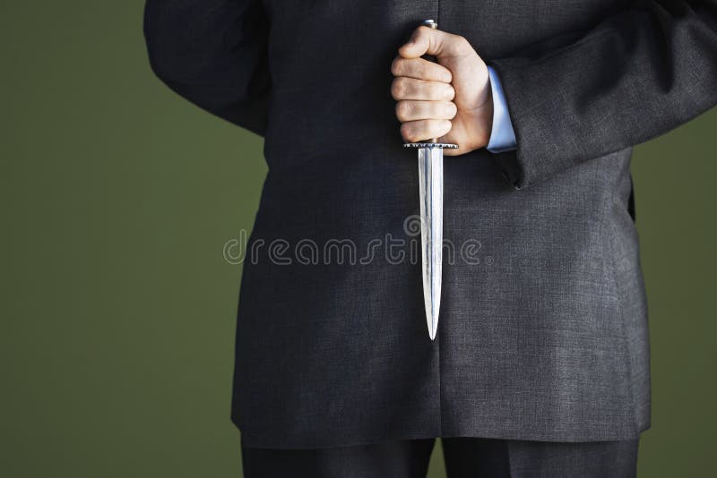 Closeup midsection of a businessman holding knife behind back against green background. Closeup midsection of a businessman holding knife behind back against green background