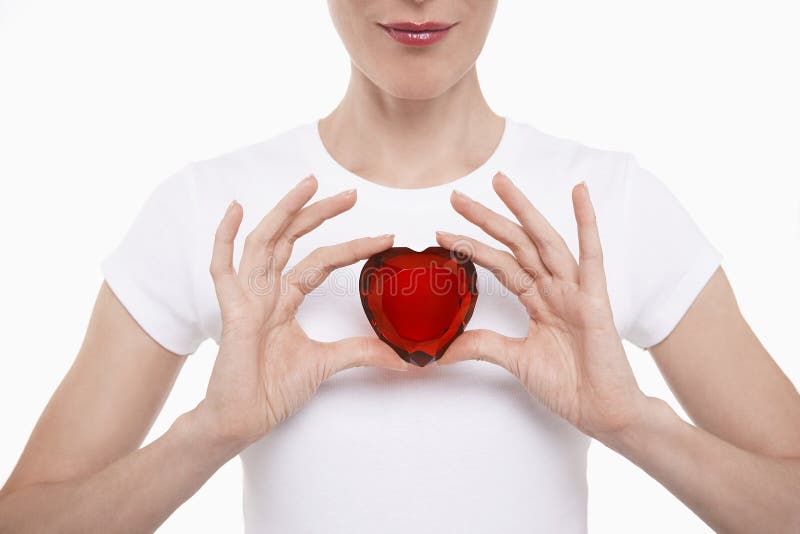 Closeup midsection of a woman in white tshirt holding red glass heart against white background. Closeup midsection of a woman in white tshirt holding red glass heart against white background